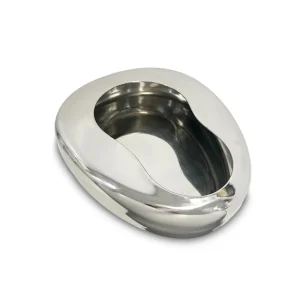 Un cuenco o chata plateada de acero con un agujero para orinar echado sobre la cama.